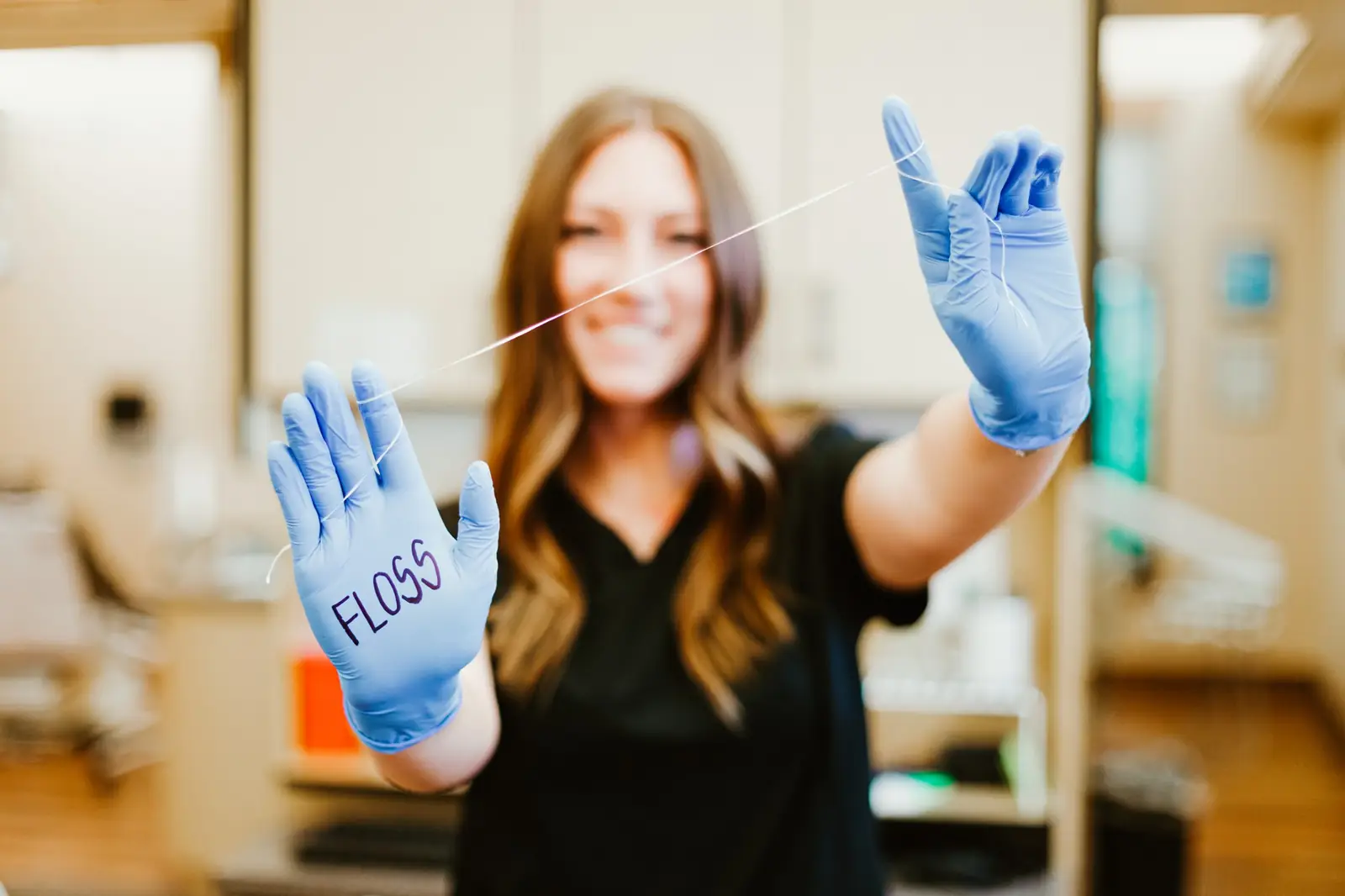 A dental professional holding dental floss with the word "FLOSS" written on their blue glove.